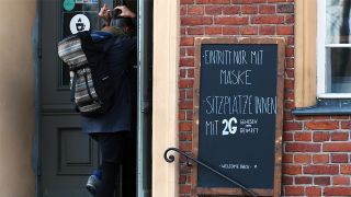 Ein Schild mit der Aufschrift "Eintritt nur mit Maske Sitzplätze innen mit 2G Genesen oder Geimpft" ist am 10.11.2021 in der Innenstadt von Potsdam neben dem Eingang zu einem Cafe angebracht. (Quelle: dpa/Soeren Stache)