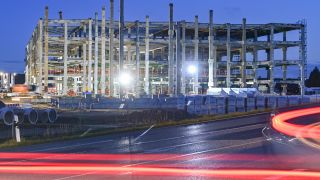 Lichtspuren vorbeifahrender Autos sind am frühen Morgen vor dem Rohbau für die künftige Batteriefabrik der Tesla-Autofarbrik zu sehen. (Quelle: Patrick Pleul/dpa)
