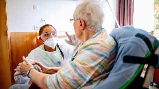Symbolbild: Eine Krankenpflegerin im Schutzanzug spricht mit einem Altenheimbewohner (Quelle: dpa/Robin Utrecht)