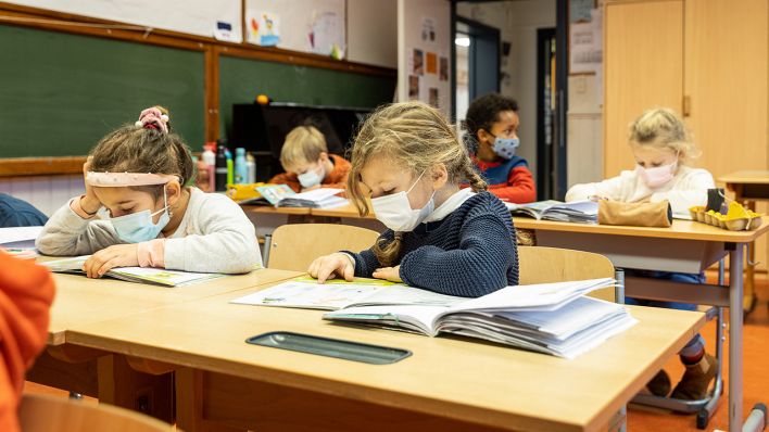 Kinder mit Mundschutz sitzen im Klassenzimmer am Schreibtisch. (Quelle: dpa/James Arthur Gekiere)