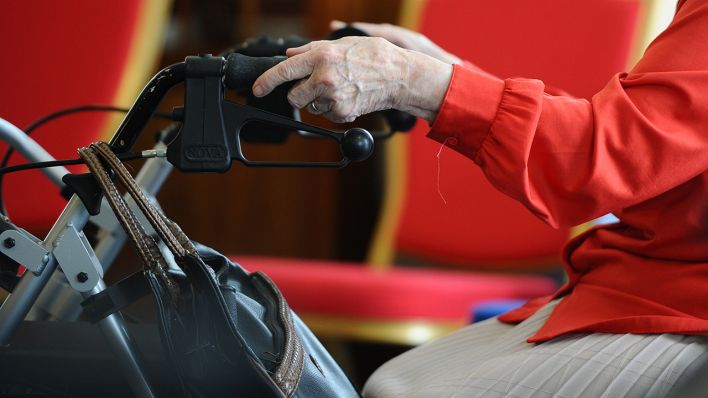 Eine ältere Person hält die Griffe eines Rollators in der Hand. (Quelle: dpa/Christoph Schmidt)