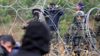 Polnische Grenzschutzbeamte stehen hinter einem Stacheldrahtzaun und bekämpfen Migranten, während sie sich an der weißrussisch-polnischen Grenze versammelt haben. Mehrere Hundert Migranten haben sich nach Angaben der Behörden in Belarus zu Fuß auf den Weg zur Grenze zum EU-Nachbarland Polen gemacht. (Quelle: Leonid Shcheglov/BelTA/AP)