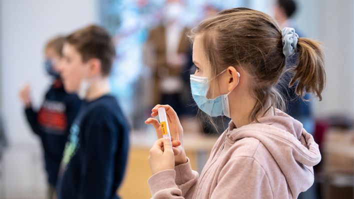 Luise (10 Jahre), Schülerin einer vierten Klasse einer Grundschule, hält während eines selbst durchgeführten Coronatests ihr Teströhrchen mit ihrer Speichelprobe in den Händen (Bild: dpa/Matthias Balk)