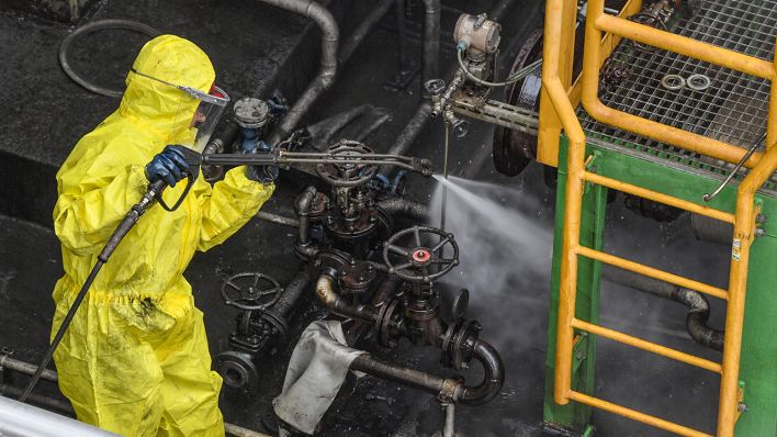 Ein Arbeiter im Schutzanzug reinigt mit Hochdruck Armaturen im Bereich der Rohöldestillation der PCK Raffinerie GmbH in Schwedt (Bild: dpa/Patrick Pleul)