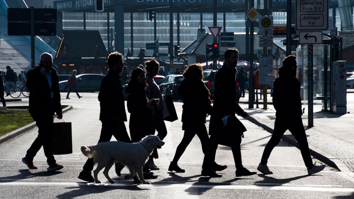 Nur als Silhouetten sind Menschen zu erkennen, die in Mitte über eine Straße gehen (Quelle: dpa/Paul Zinken)
