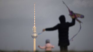 Ein Erwachsener und ein Kind zeichnet sich ab beim Drachensteigen mit Blick auf den Berliner Fernsehturm in Berlin (Quelle: imago images/Florian Gaertner)