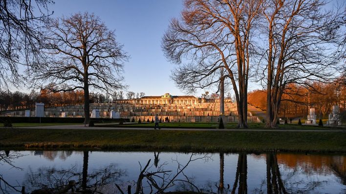 Im Park Sanssouci ist das Schloss Sanssouci am späten Nachmittag im Licht der untergehenden Sonne zu sehen und spiegelt sich in einem Gewässer. (Quelle: dpa/Jens Kalaene)