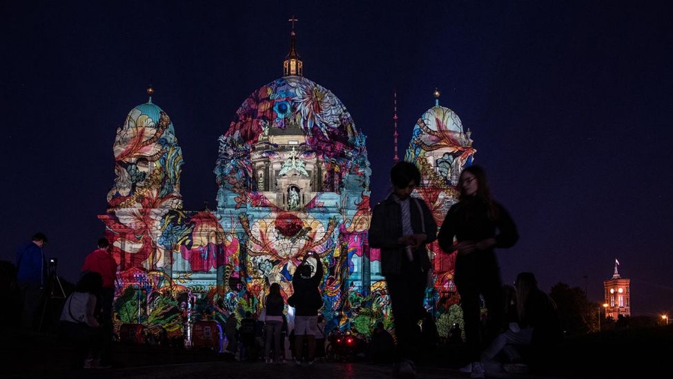 Menschen stehen zum Auftakt des 17. Festival of Lights vor dem illuminierten Berliner Dom. (Quelle: dpa/Paul Zinken)
