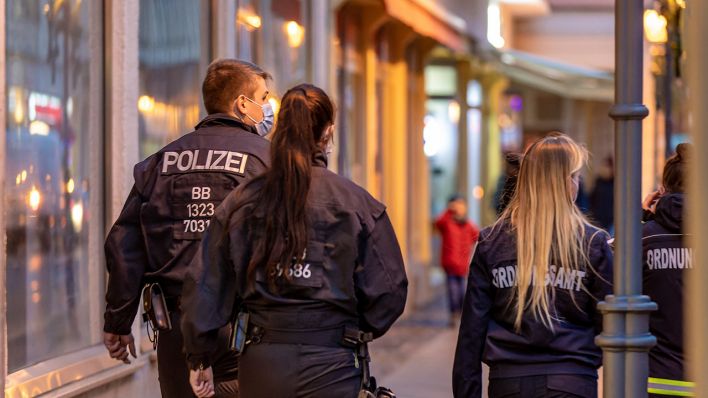 Mitarbeiterinnen des Ordnungsamts und ein Polizeibeamter laufen die Berliner Straße in Cottbus entlang. (Quelle: dpa/Frank Hammerschmidt)