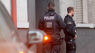 Symbolbild: Polizisten stehen vor einem Haus, in dem sie eine Wohnung durchsucht haben. (Quelle: dpa/R. Weihrauch)