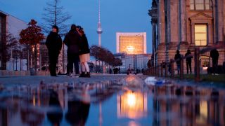 Passanten stehen am Abend neben dem Reichstagsgebäude (r) vor dem Berliner Fernsehturm. (Quelle: dpa/Christoph Soeder)