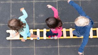 Kinder balancieren auf dem Spielplatz einer Kindertagesstätte auf einem Brett. (Quelle: dpa/Sebastian Kahnert)