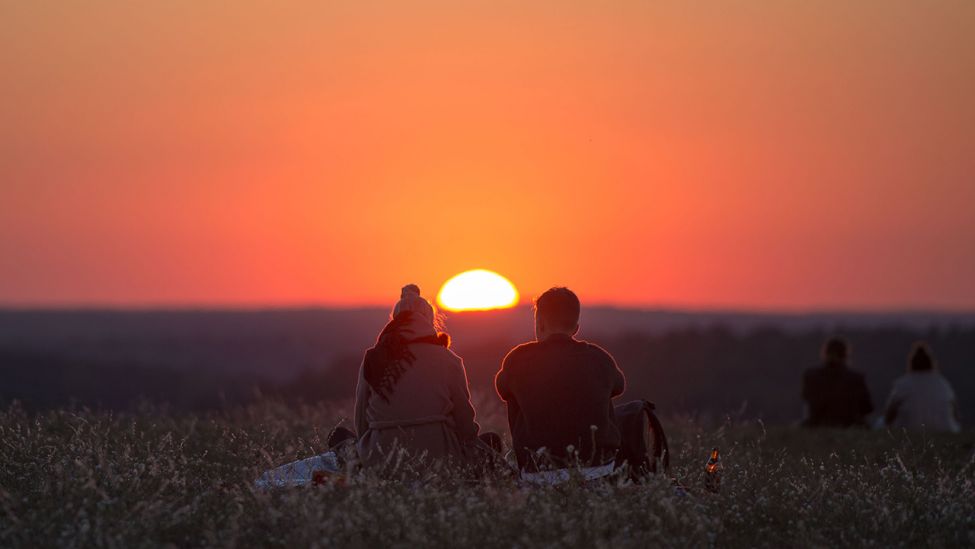 Ein Mann und eine Frau sitzen auf dem Drachenberg in Berlin und genießen den Sonnenuntergang. (Quelle: dpa/Lukas Schulze)
