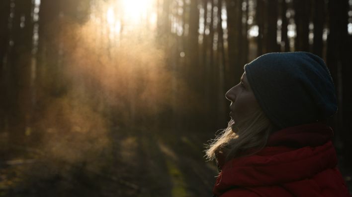 Eine Frau steht im kalten Wetter im Gegenlicht in einem Wald und man sieht ihren warmen Atem (Quelle: DPA/Patrick Pleul)