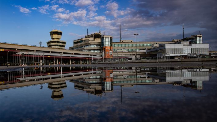 Die Gebäude des ehemaligen Flughafen Tegel spiegeln sich in einer Wasserpfütze (Bild: dpa/Paul Zinken)