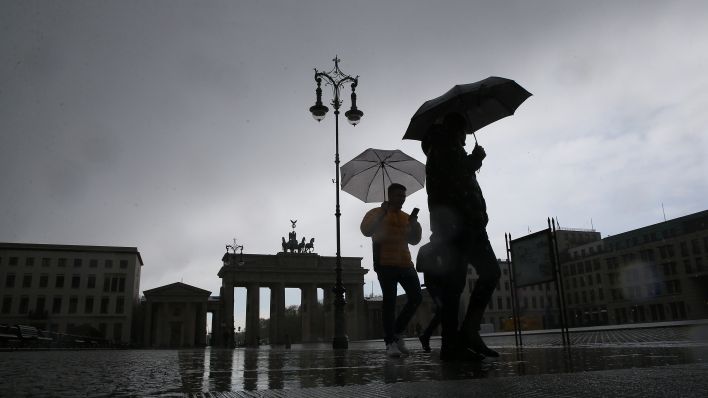 Bei Temperaturen um vier Grad Celsius und heftigen Regenschauern gehen Menschen mit Regenschirmen vor dem Brandenburger Tor über den Pariser Platz. (dpa/Wolfgang Kumm)