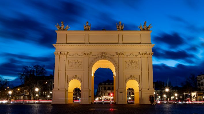 Das beleuchtete Brandenburger Tor zeichnet sich vor dem Abendhimmel ab. Im Hintergrund ziehen Scheinwerfer und Rückleuchten vorbeifahrender Autos Lichtspuren durch die Dunkelheit (Aufnahme mit Langzeitbelichtung). (Quelle: dpa/Monika Skolimowska)