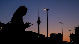 Eine Frau schaut am Abend vor dem Berliner Fernsehturm an der Karl-Marx-Allee auf ihr Handy. (Quelle: dpa/Christoph Soeder)