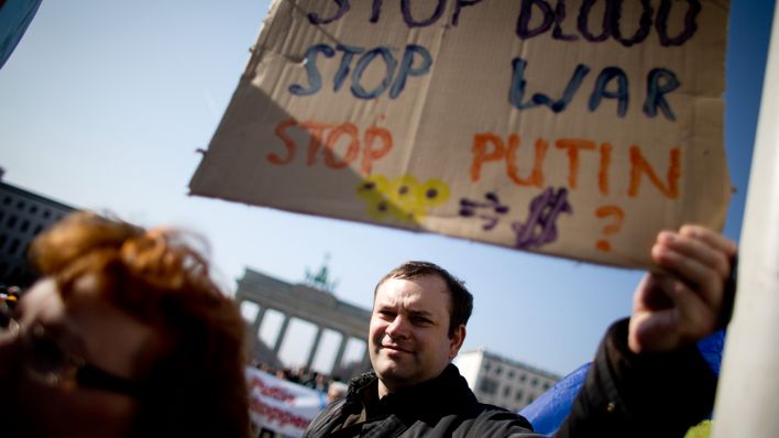 Menschen stehen am Brandenburger Tor und halten ein Plakat mit der Aufschirft "Stop Blood, Stop War, Stop Putin". (Quelle: dpa/Kay Nietfeld)