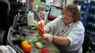 Ein Kassiererin wiegt an der Kasse in einem Supermarkt Gemüse. (Quelle: dpa/Oliver Berg)