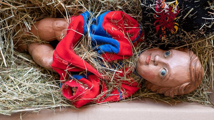 Archivbild: Eine Christkind-Figur aus Lindenholz liegt auf Heu in einem Paket. (Quelle: dpa/C. Lohse)