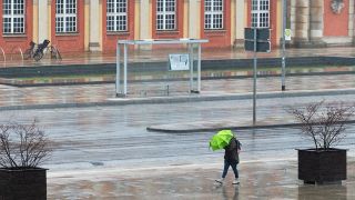 Eine Frau schützt sich vor der Kulisse des Filmmuseums mit einem grünen Schirm vor Regen und Wind. (Quelle: dpa/Soeren Stache)