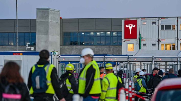 Arbeiter warten am frühen Morgen an einem Eingang zur Baustelle für die Tesla-Autofabrik. (Quelle: dpa/Patrick Pleul)