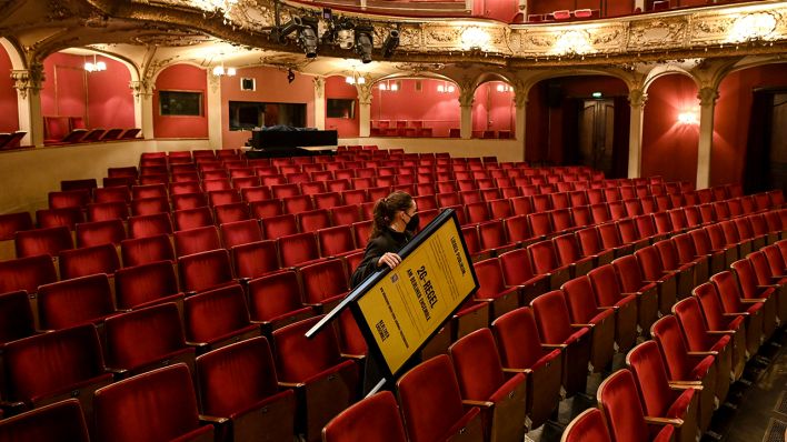 Eine Mitarbeiterin trägt einen Aufsteller mit dem Hinweis auf die 2G-Regel durch den Zuschauerraum des Berliner Ensemble. (Quelle: dpa/Britta Pedersen)