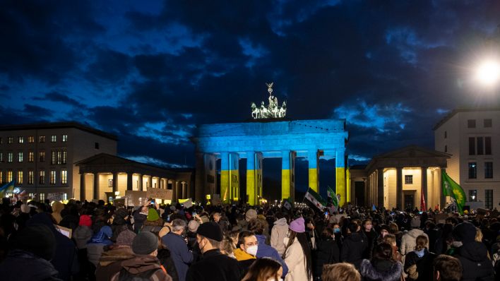 Während einer Demonstration in Berlin gegen den Krieg in der Ukraine wird das Brandenburger Tor in den ukrainischen Nationalfarben angeleuchtet. (Quelle: dpa/Paul Zinken)