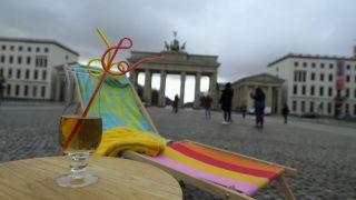 Ein Liegestuhl mit Handtüchern und ein Tisch mit Cocktail stehen vor dem Brandenburger Tor. (Bild: rbb)