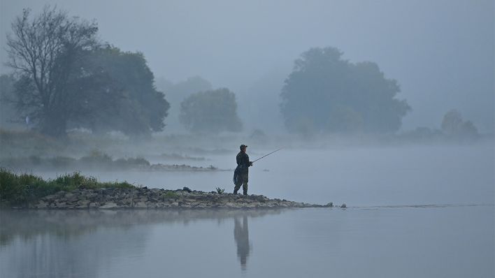 Ein Angler steht im Morgennebel kurz vor Sonnenaufgang im Oktober 2021 auf einer Buhne am deutsch-polnischen Grenzfluss Oder. (Quelle: dpa/Patrick Pleul)