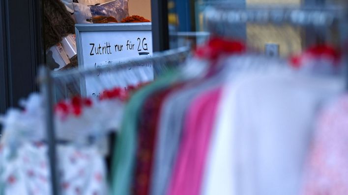 An einem Kleidungsgeschäft steht ein Hinweisschild mit der Aufschrift „Zutritt nur 2G“ im Potsdamer Stadtteil Babelsberg. (Quelle: dpa/Britta Pedersen)