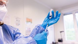 Eine Mitarbeiterin des Impfzentrums im Kreis Warendorf, hält ein Fläschchen (Phiole) mit dem Impfstoff Nuvaxovid des Pharmaunternehmens Novavax und eine Spritze in den Händen. (Quelle: Guido Kirchner/dpa)
