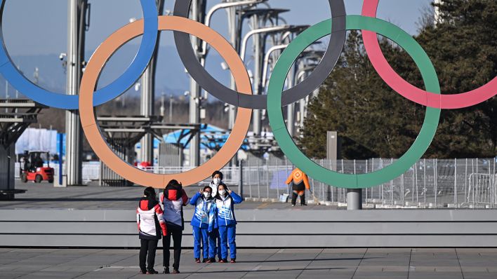 Volunteers stehen für ein Selfie vor den olympischen Ringen in Peking (Bild: dpa/Peter Kneffel)
