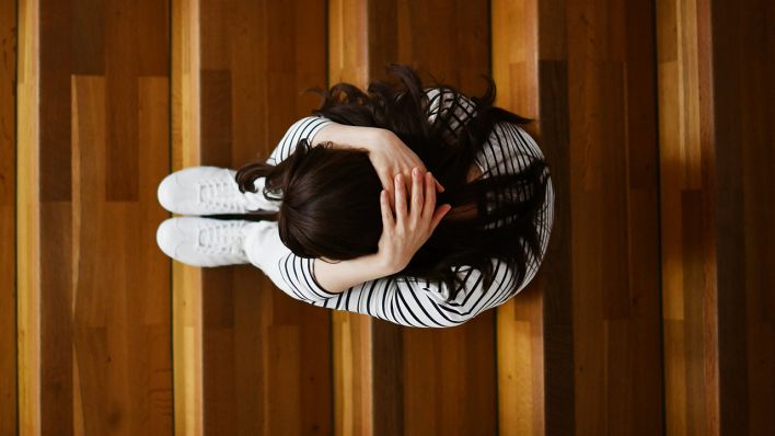 Symbolbild: Ein Mädchen sitzt mit hinter dem Kopf verschränkten Händen auf Treppenstufen. (Quelle: dpa/F. May)