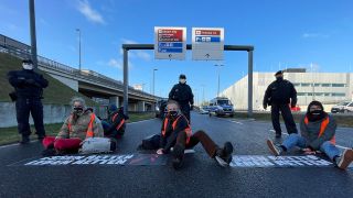 Klimaschutz-Aktivisten der Initiative "Aufstand der letzten Generation" blockieren eine Zufahrt zum Hauptstadt-Flughafen BER. Auf dem Boden liegen Banner mit der Aufschrift «Essen retten, Leben retten». (Quelle: dpa/P. Zinken)