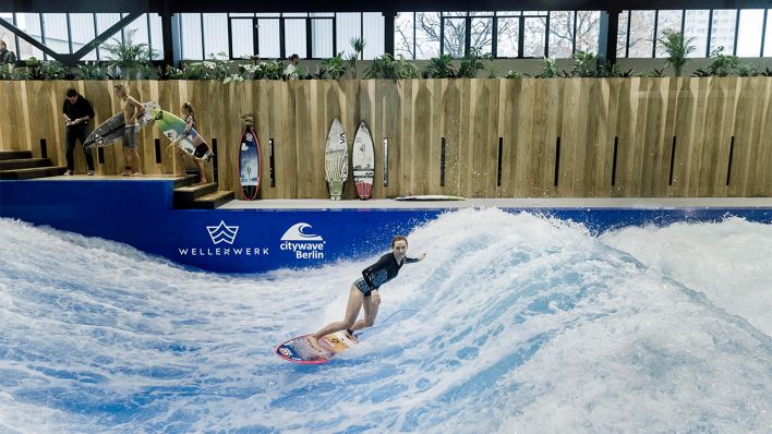 Eine Surferin springt am 20.11.2019 auf einer künstlichen Surfwelle in der Indoor-Surfhalle Wellenwerk. (Quelle: dpa/Carsten Koall)