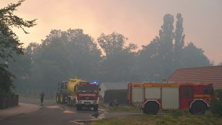 Einsatzfahrzeuge der Feuerwehr werden betankt, während dichter Rauch die Sonne verdeckt. (Quelle: dpa/J. Carstensen)