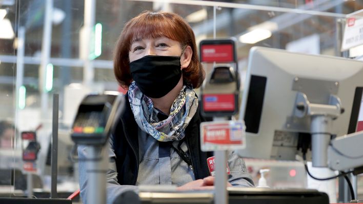 Kassiererin Kerstin Strasen lächelt unter ihrer Maske an der Kasse eines Supermarktes. (Quelle: dpa/Michael Sohn)