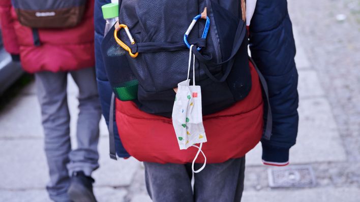 Eine Kindermaske hängt an einem Rucksack eines Schulkindes. (Quelle: dpa/Annette Riedl)