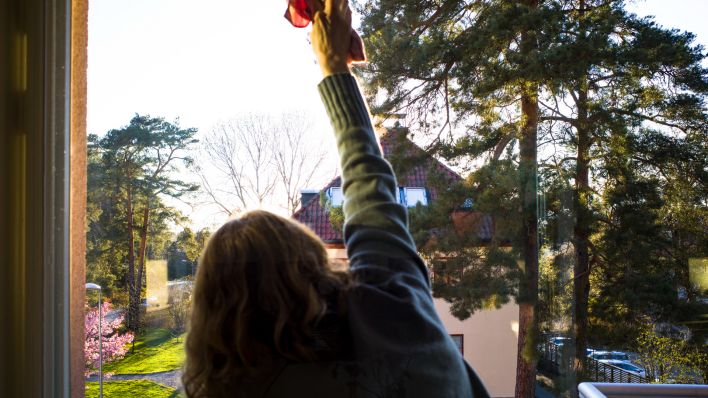 Eine Frau putzt eine Fensterscheibe in einem Wohnhaus. (Quelle: dpa/Alexander Farnsworth)
