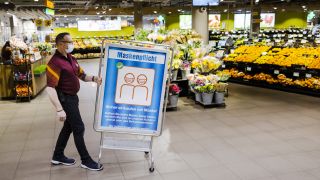 Ein Mitarbeiter eines Lebensmittelmarktes verschiebt ein Hinweisschild zur Maskenpflicht. (Quelle: dpa/Michael Buholzer)