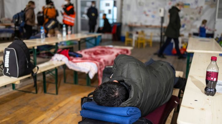 Ein Mann schläft in einem Zelt für Geflüchtete aus der Ukraine vor dem Hauptbahnhof auf Bierbänken. (Quelle: dpa/Michael Hanschke)