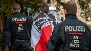 Ein Demonstrant mit einer schwarz-weiß-roten Flagge mit einem Eisernen Kreuz darauf wird von zwei Polizisten abgeführt. (Quelle: dpa/Christophe Gateau)