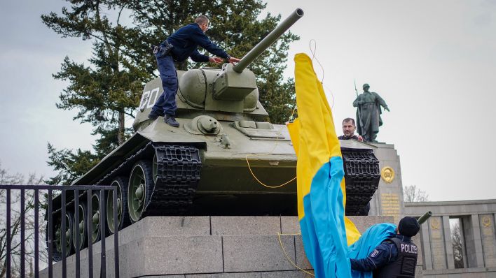 Polizeibeamte entfernen die Flagge der Ukraine von einem historischen Panzer am Sowjetischen Ehrenmal an der Straße des 17. Juni. Zuvor war der Panzer in die ukrainische Flagge gehüllt. (Quelle: dpa/K. Nietfeld)