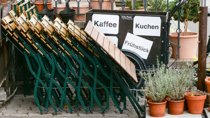 Tische und Klapptsühle eines Cafes stehen zusammenklappt in einer Ecke (Bild: dpa/Jens Kalaene)