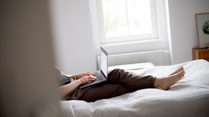 Symbolbild: Eine Frau sitzt auf einem Bett und arbeitet mit ihrem Laptop, aufgenommen am 17.01.2022 in Berlin (gestellte Szene). (Quelle: dpa/Zacharie Scheurer)