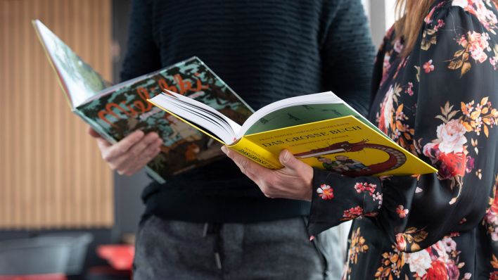 Eine Frau und ein Mann halten vor dem Start des Vorlese-Weltrekordversuchs der LeseLounge e.V. Kinderbücher in den Händen. (Quelle: dpa/Paul Zinken)