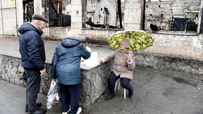 Die siebzigjährige Tetiana Koronik (r) verkauft Milch und Käse vor einem zerstörten Gebäude auf dem Makariw-Platz (Bild: dpa/Jussi Nukari)