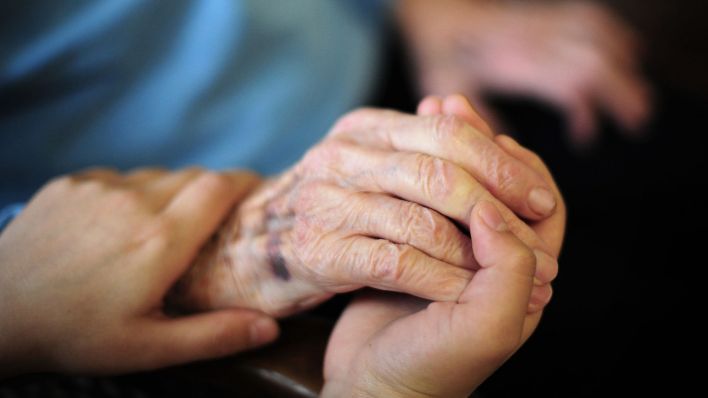 Eine Pflegekraft hält in einem Seniorenheim die Hand einer Bewohnerin. (Quelle: dpa/Daniel Reinhardt)